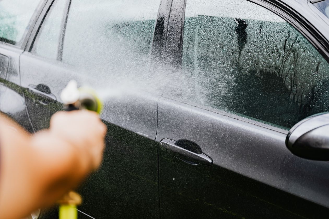 Mão lavando carro com mangueira no pátio